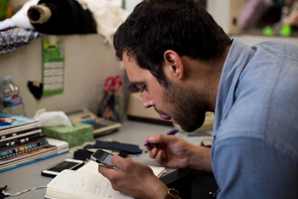 Victor Kali at work, measuring with a phone and his engineering journal at a desk.