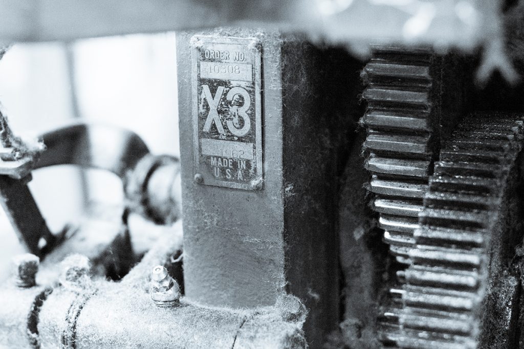 A black and white close up view of our restored Draper X3 shuttle loom, including distinct nameplate and loom gears.