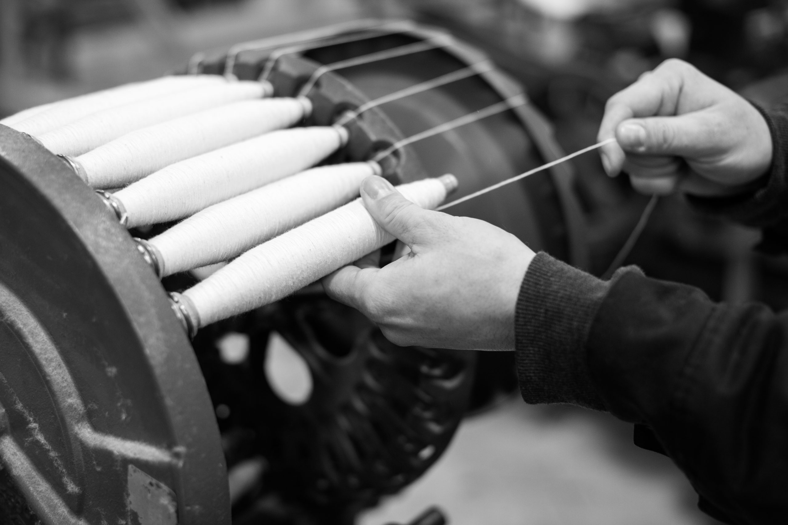 black and white photo craftsman hands working with shuttle loom bobbins wound with white cotton yarn