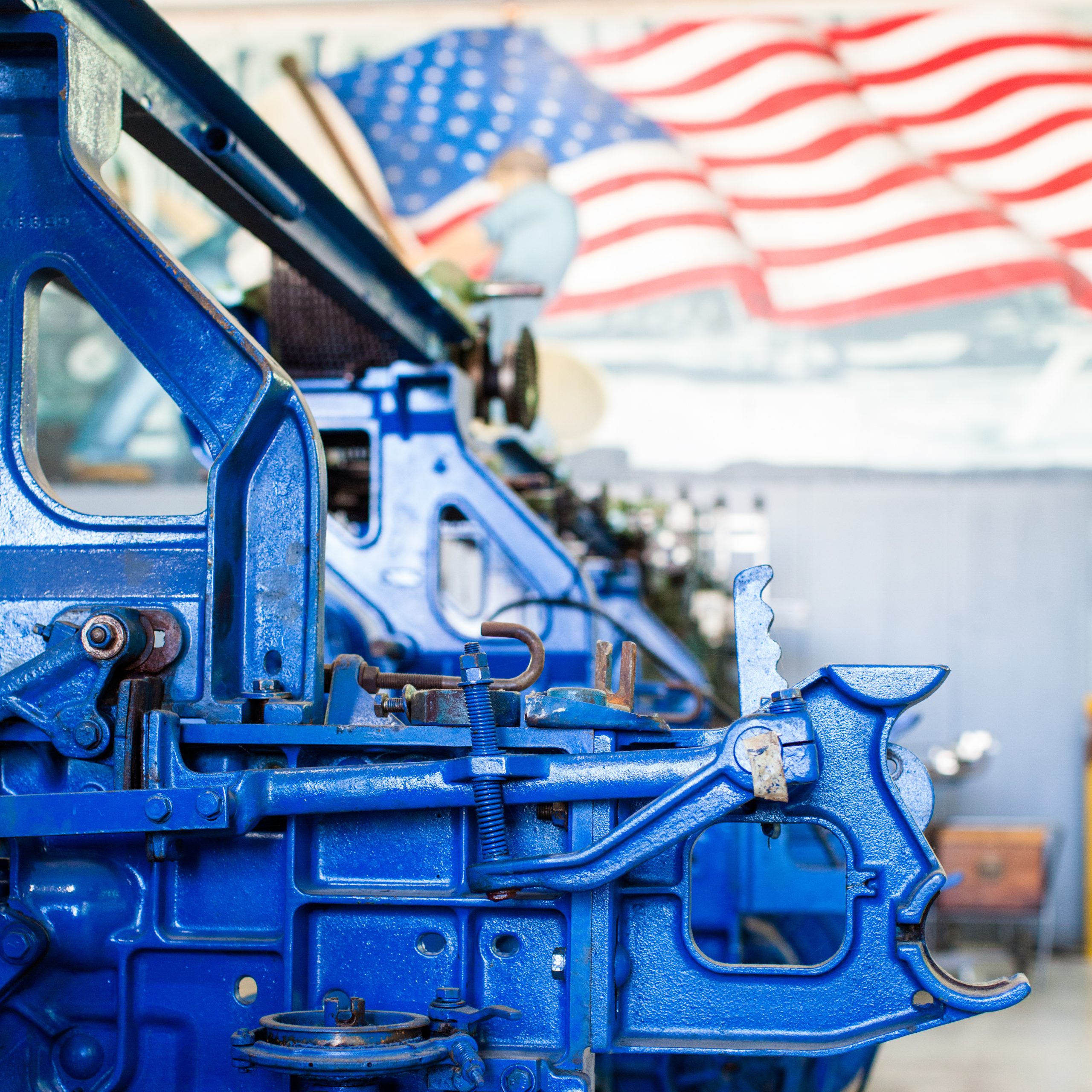 color photograph with vivid blue Toyoda industrial loom in forefront and american flag worker mural in background