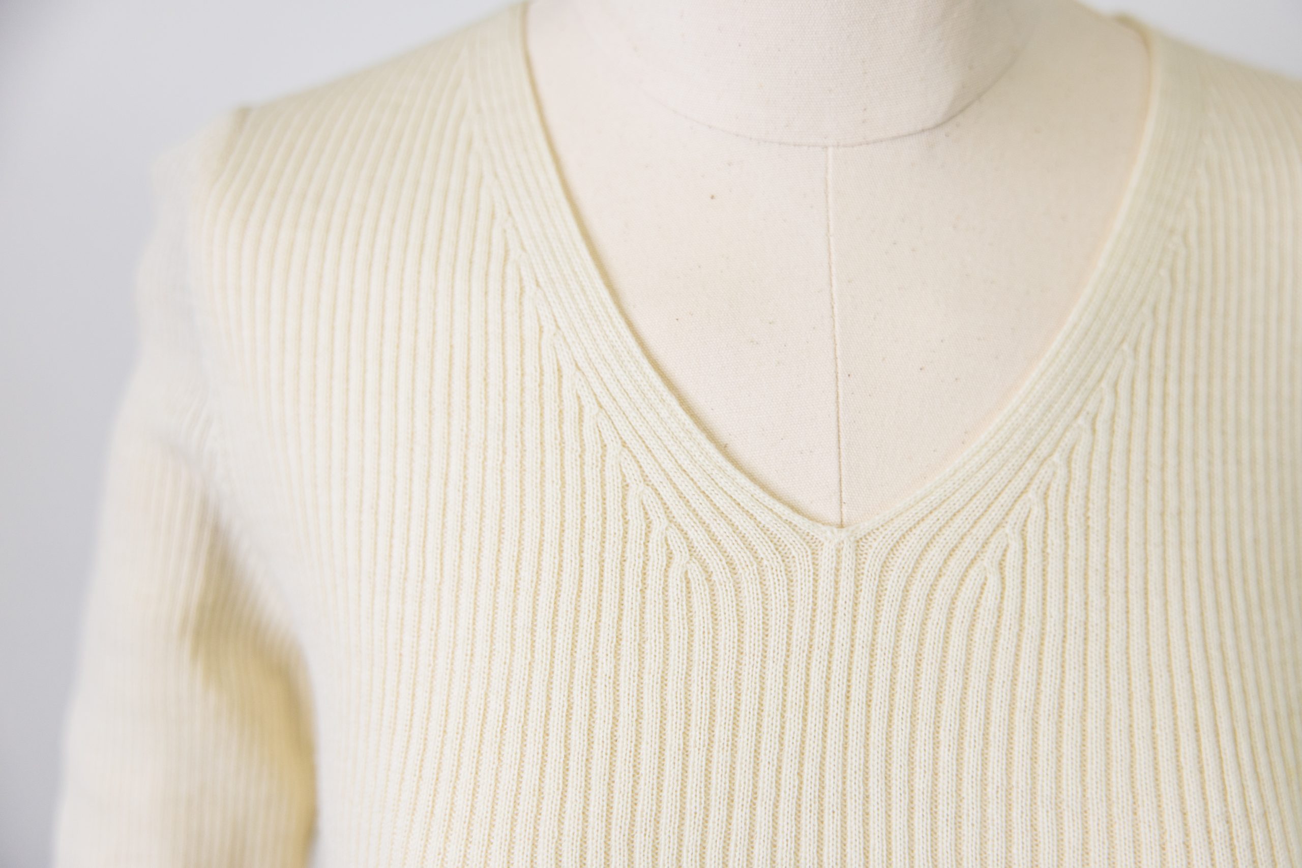 Detailed photograph of a fine knit wool rib sweater v-neck on a mannequin