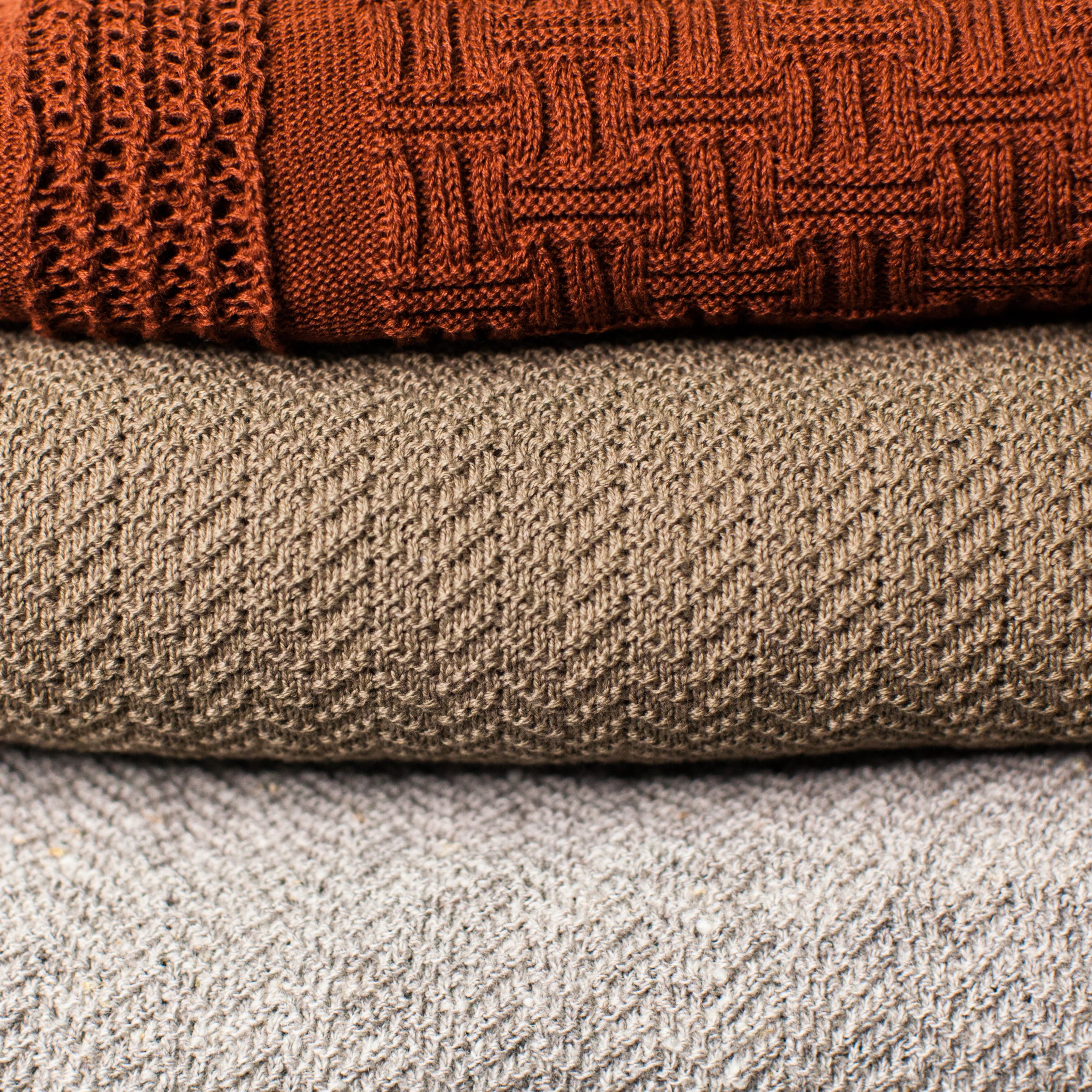 Fine knit cotton blankets stacked with a red complex knit pattern on top of a brown and grey mock herringbone construction
